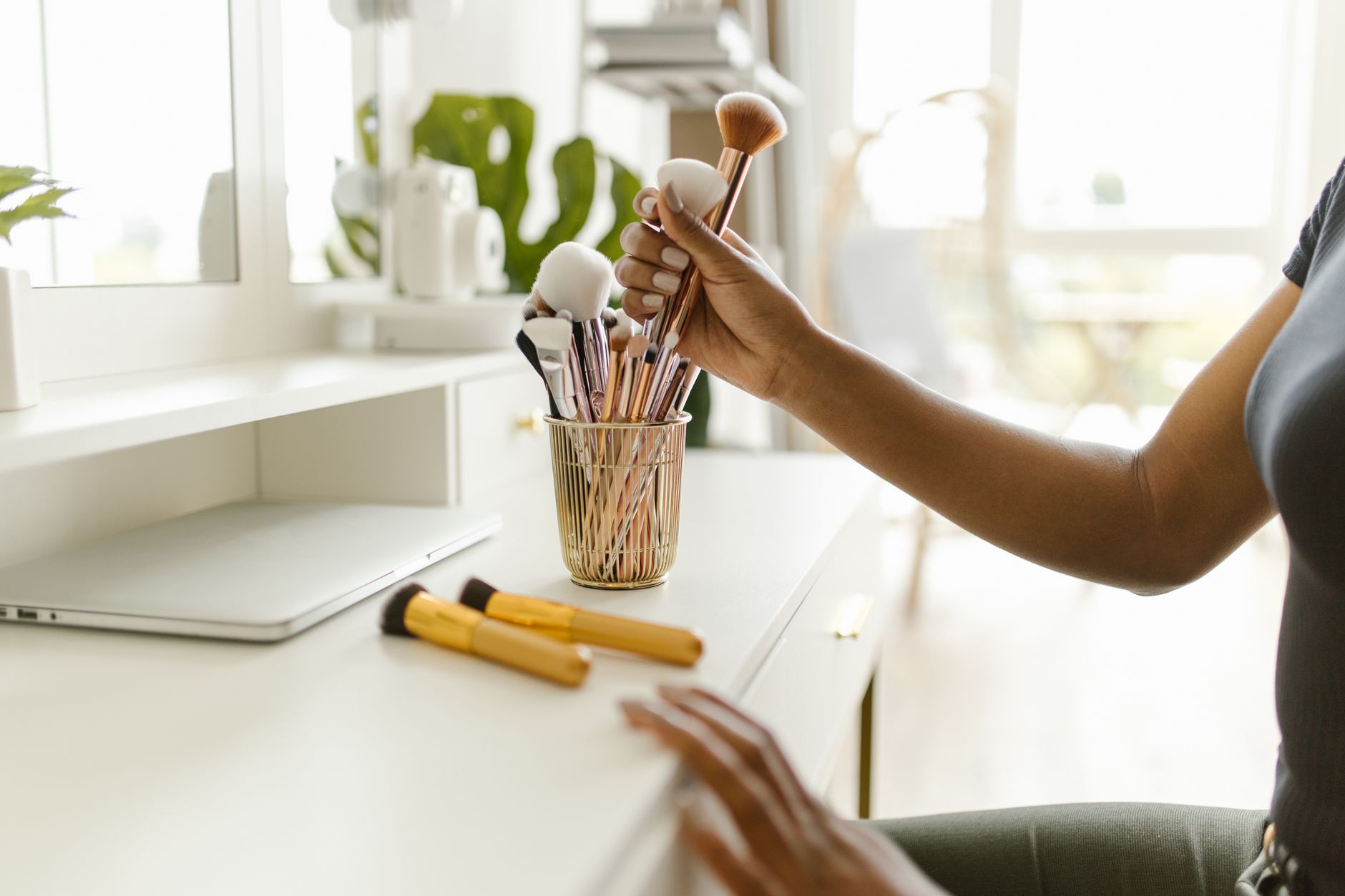 A woman organizing makeup brushes on a white dresser in a bright and modern room.