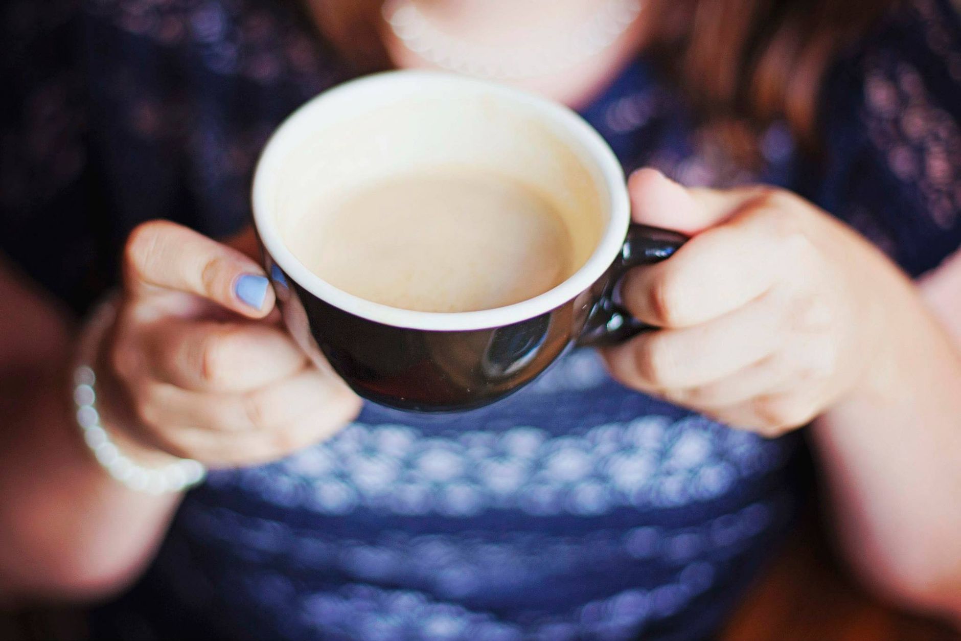 A close-up shot of a woman holding a warm cappuccino cup indoors.