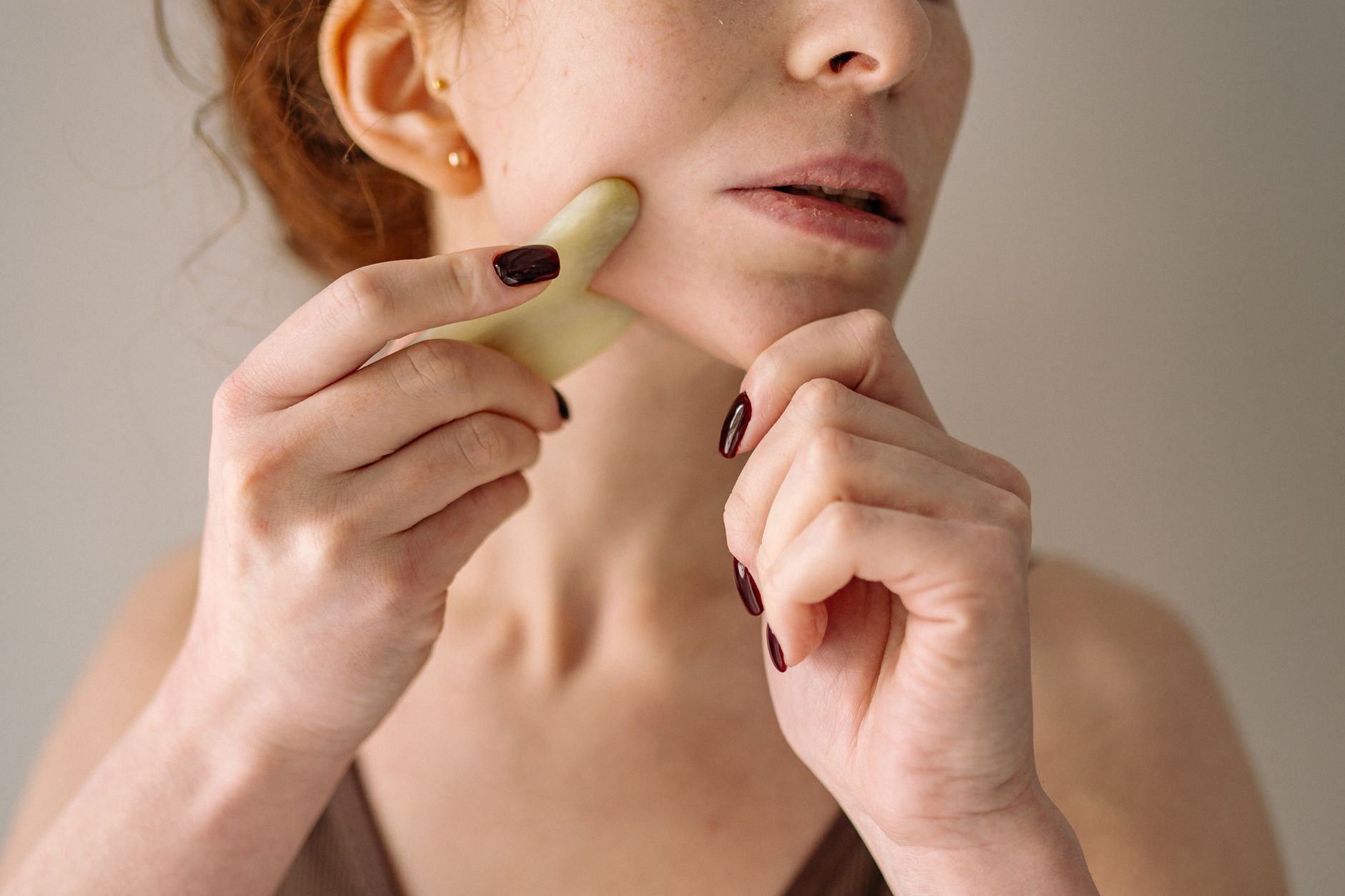 Close-up of a woman using a gua sha stone on her face, emphasizing self-care and beauty routine.