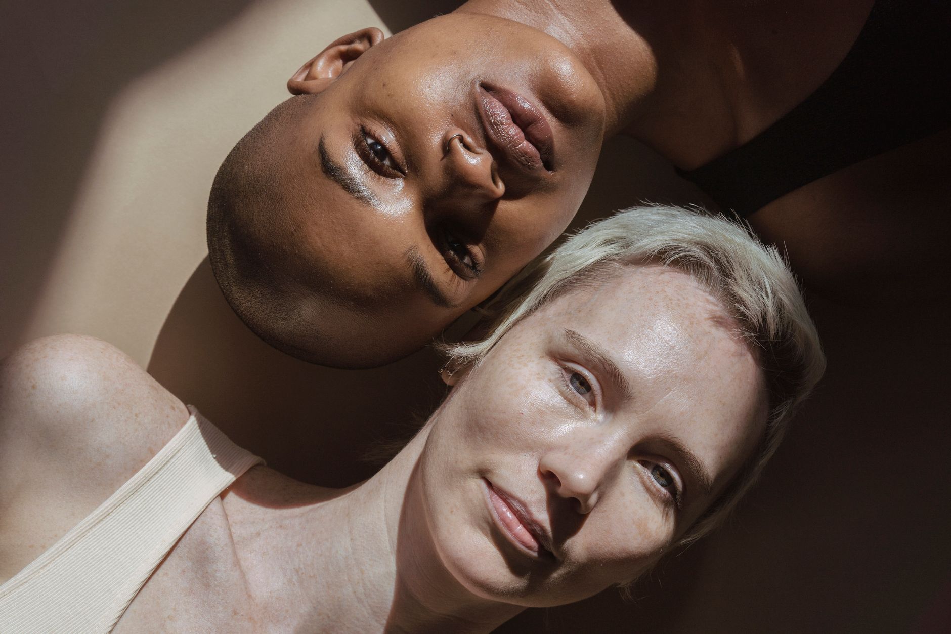 Top view of portrait of calm diverse women without makeup lying on gray surface and looking at camera