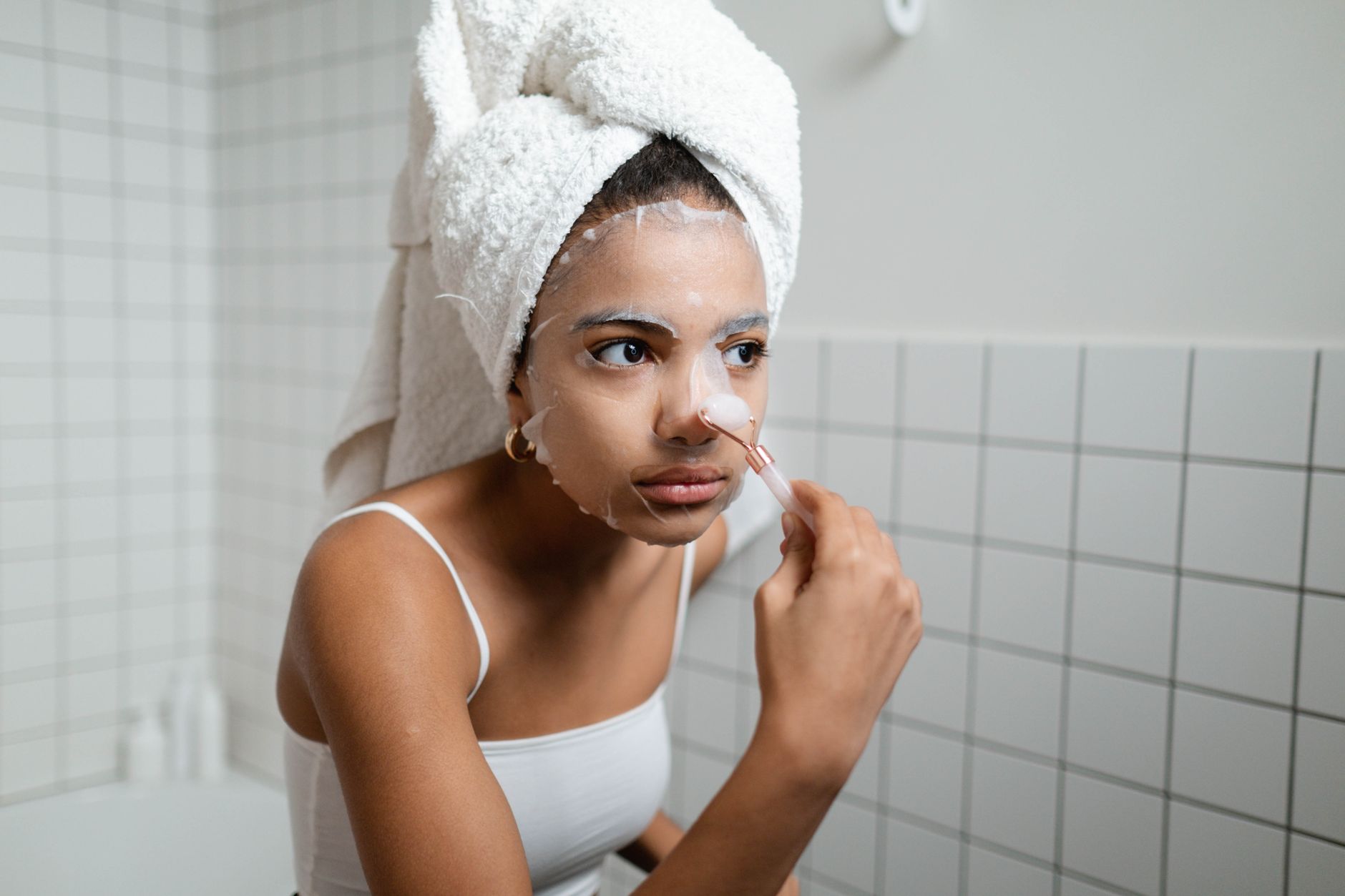 A young woman applying a facial cosmetic mask in a modern bathroom, engaging in a beauty routine.