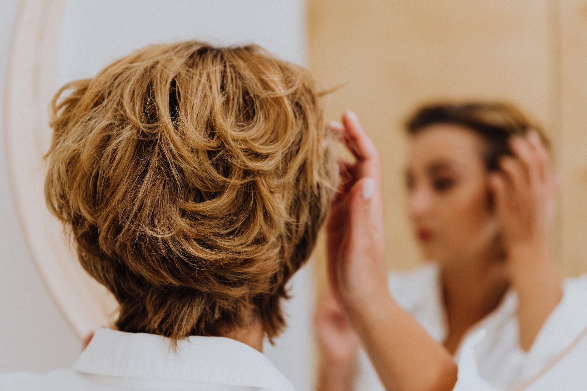 Back view of a woman styling her short hair while looking in the mirror.