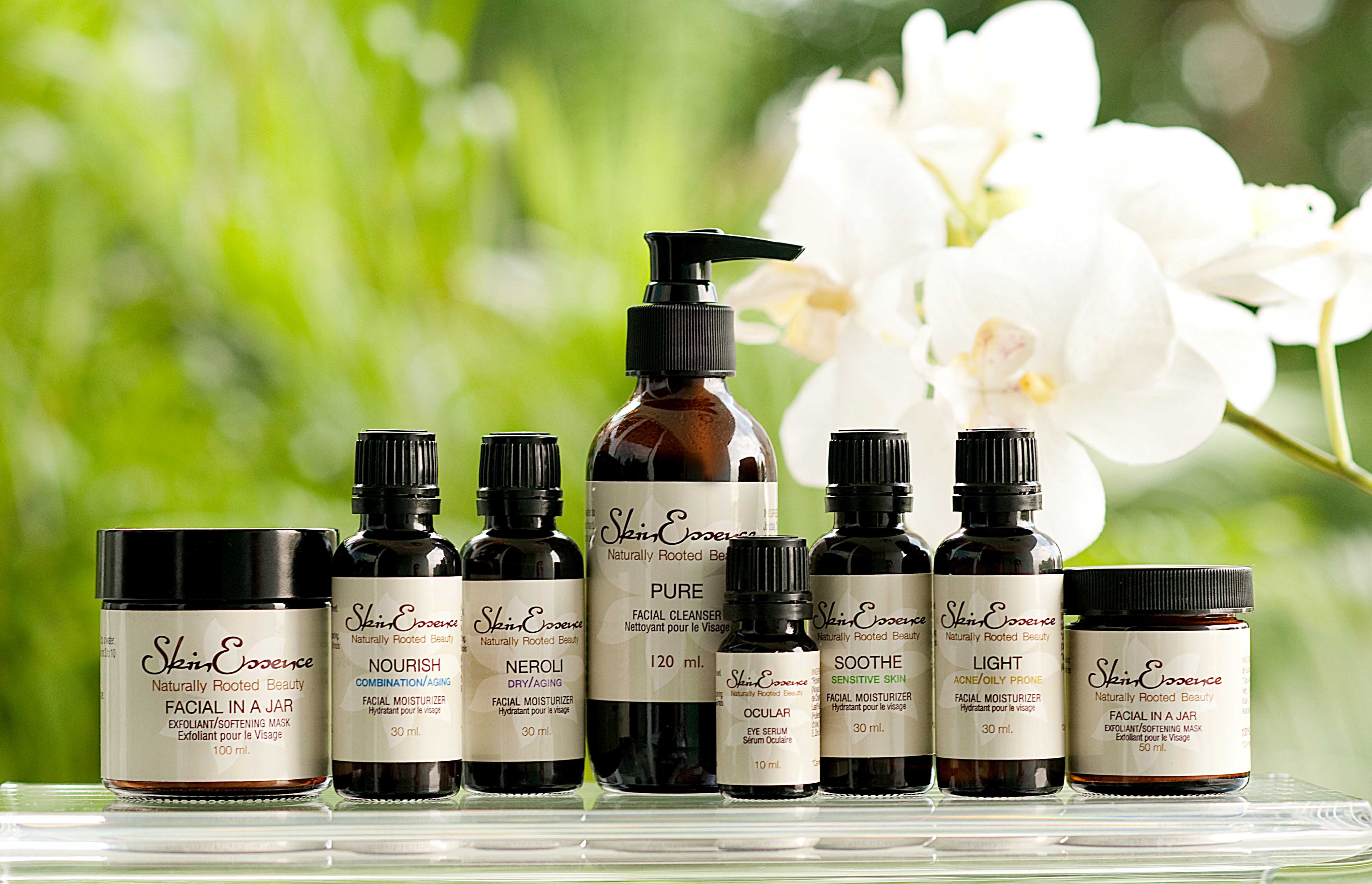  A variety of skincare products, including a facial cleanser, moisturizer, eye serum, and face mask, are displayed on a shelf with a white flower in the background.